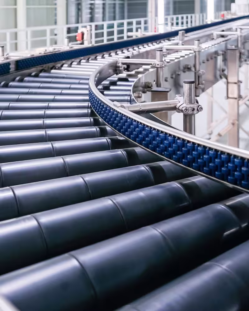 Industrielles Fördersystem mit Rollenspuren und gekrümmtem blauen Antriebsriemen in Fabrik